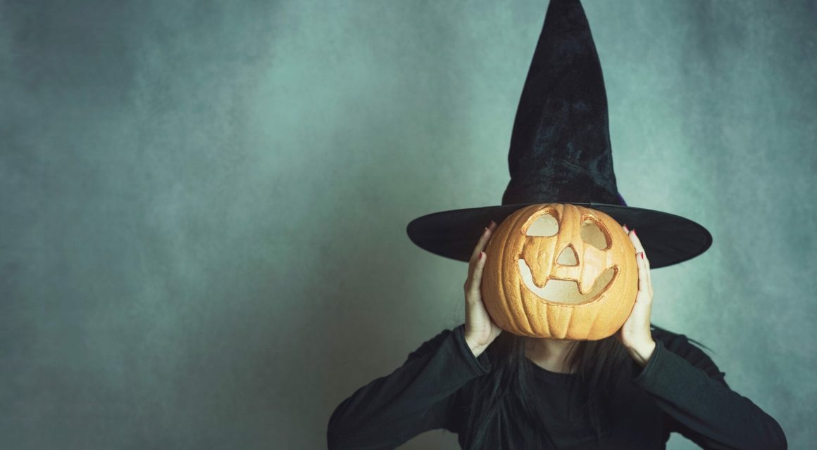 Woman Wearing Costume Covering Face With Jack O Lantern Against Wall During Halloween