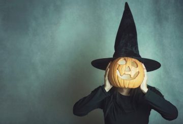 Woman Wearing Costume Covering Face With Jack O Lantern Against Wall During Halloween