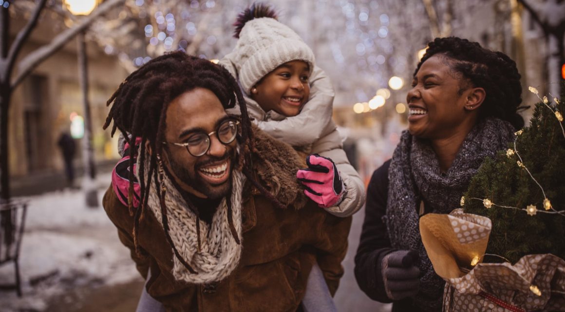 Young family preparing for Christmas holiday. They walking on street and carrying Christmas stuff.