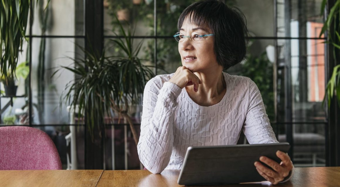 woman in her 60s using tablet with hand on chin