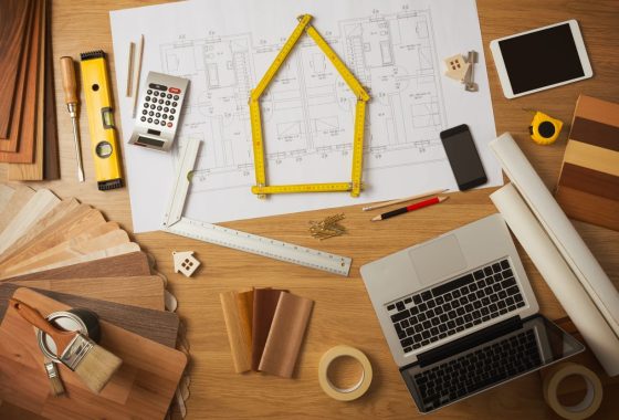 Architect and home interior decorator desktop with tools, laptop, wood swatches and home project draft top view, a meter is composing a house at center