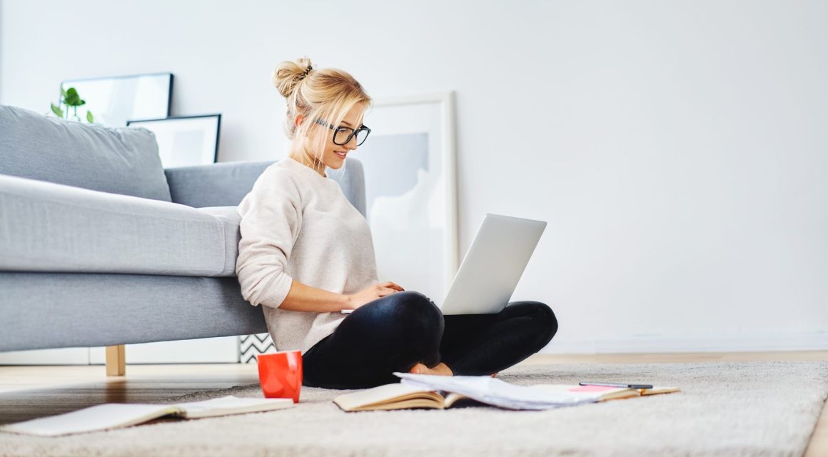 Female student sitting on floor of her apartment with laptop
