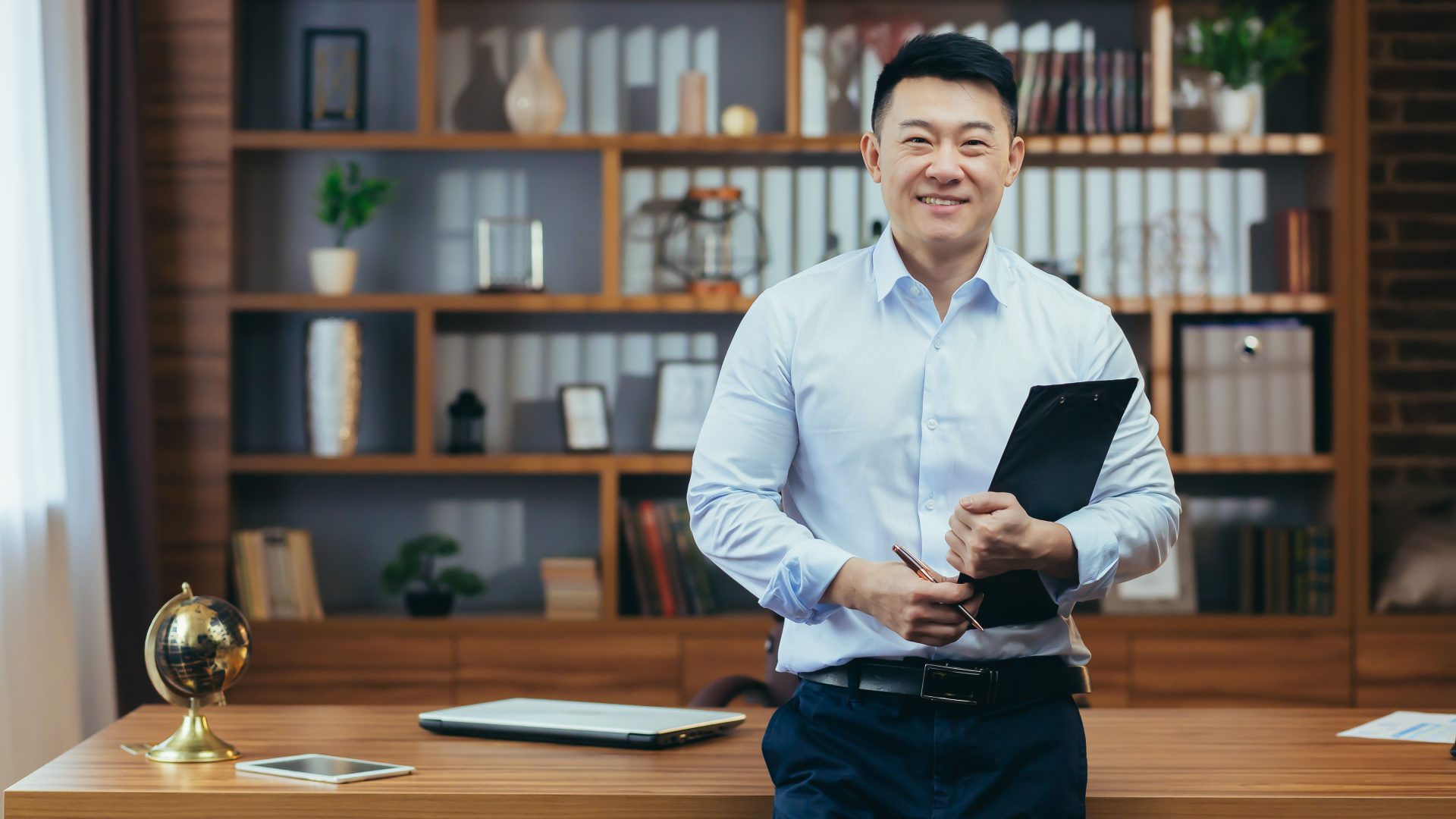 Portrait of a successful financier, Asian in a shirt looks at the camera and smiles in a classic office