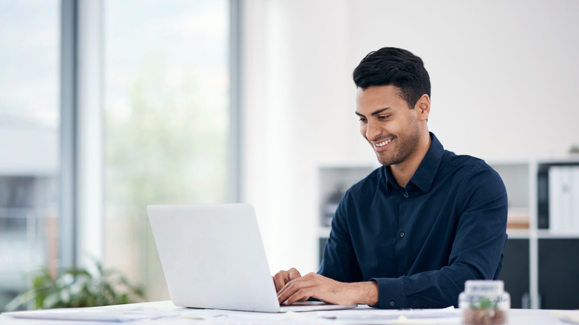 Shot of a young businessman using a laptop at his desk in a modern office