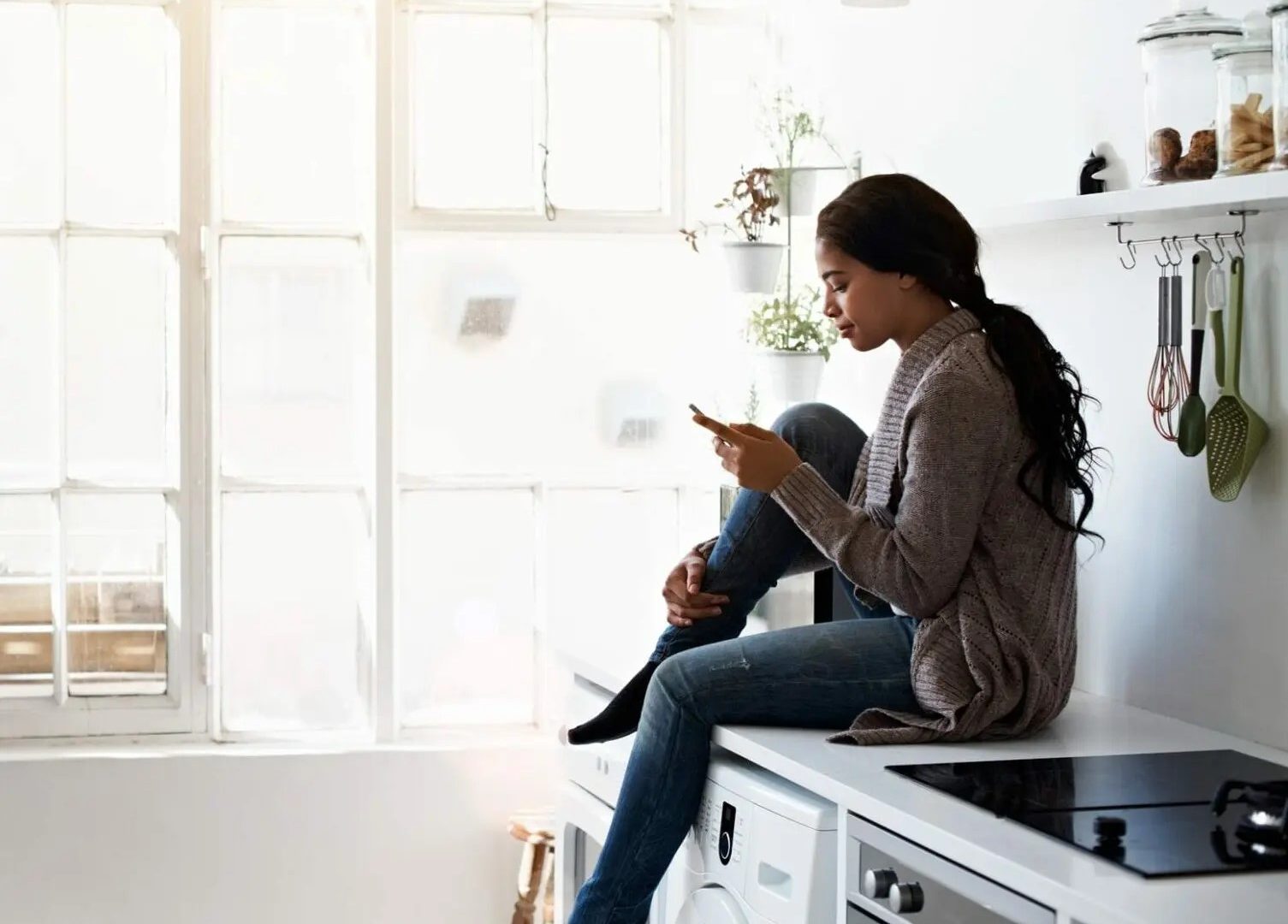 woman sitting on washing machine looking at phone