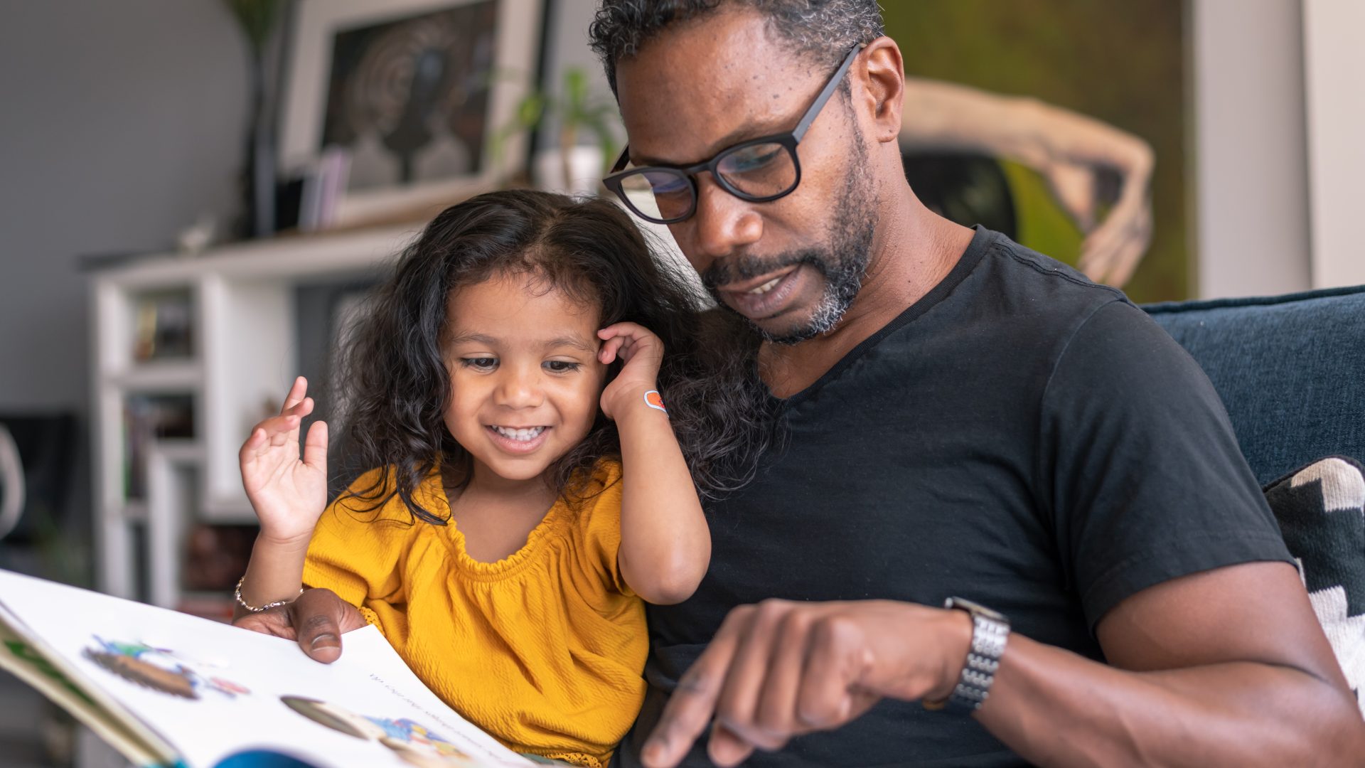 Affectionate father reading book with adorable mixed race daughter