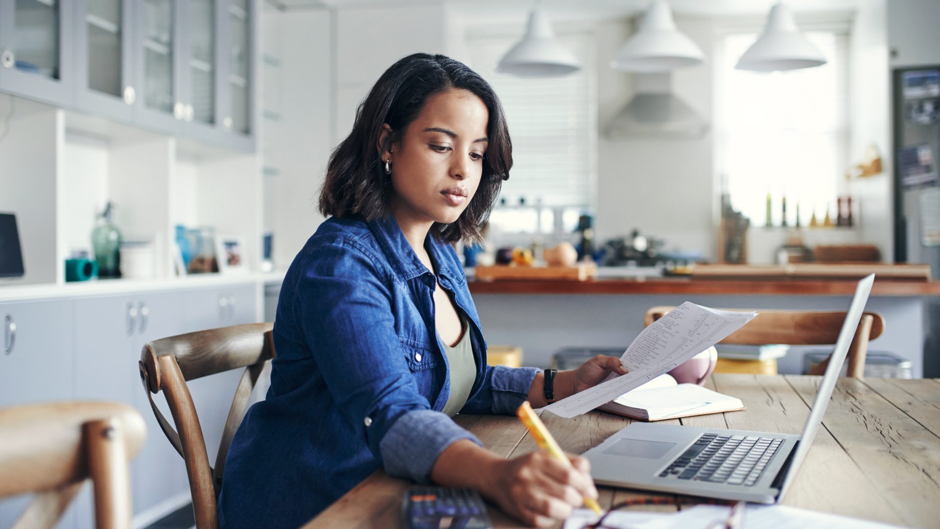 Shot of a young woman using a laptop and going through paperwork while working from home