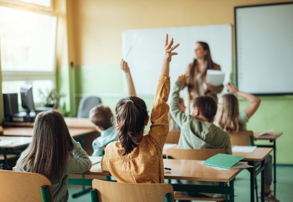 Students raising hands while teacher asking them questions in classroom