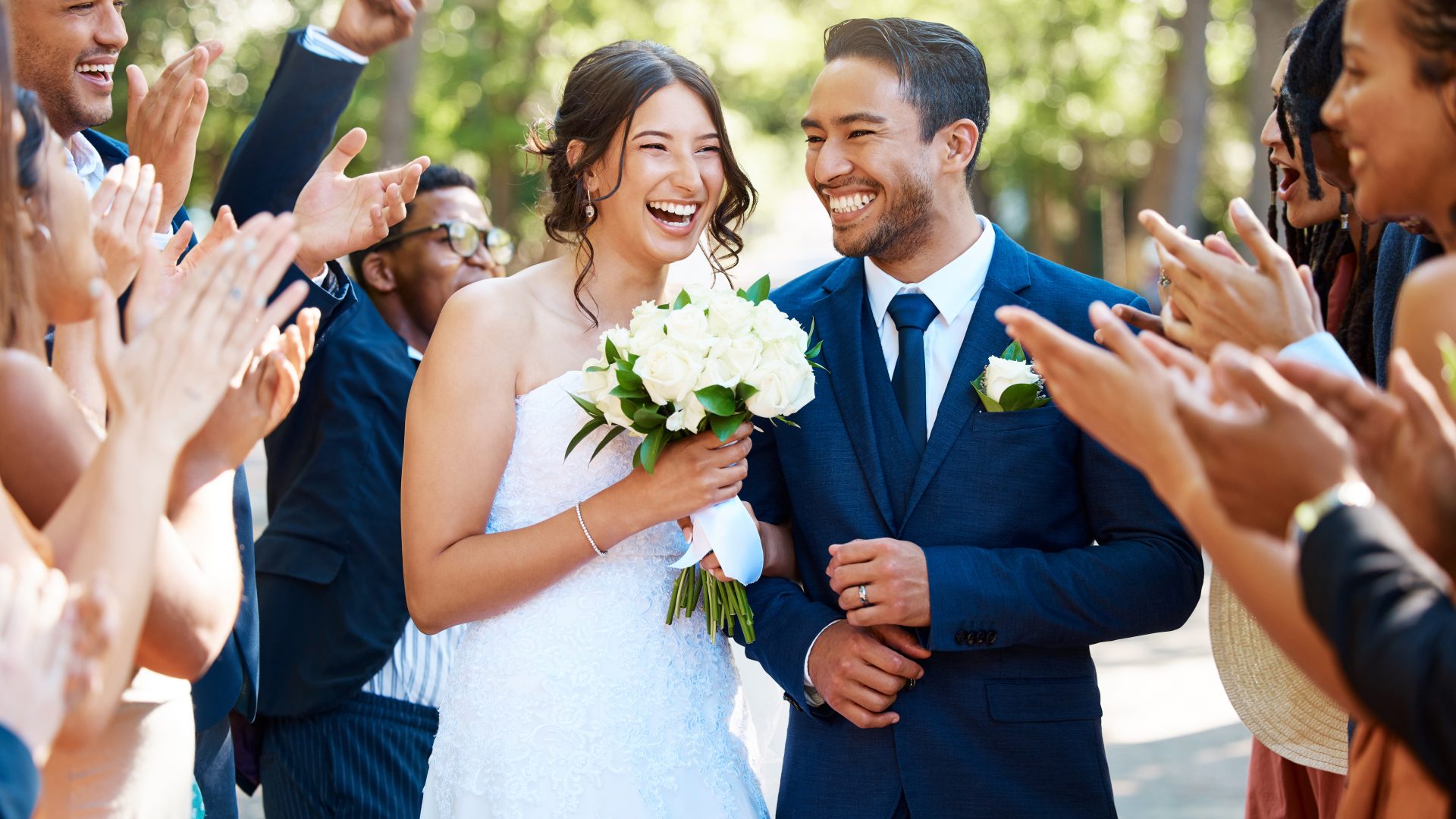 Wedding guests clapping hands as the newlywed couple walk down the aisle. Joyful bride and groom walking arm in arm after their wedding ceremony