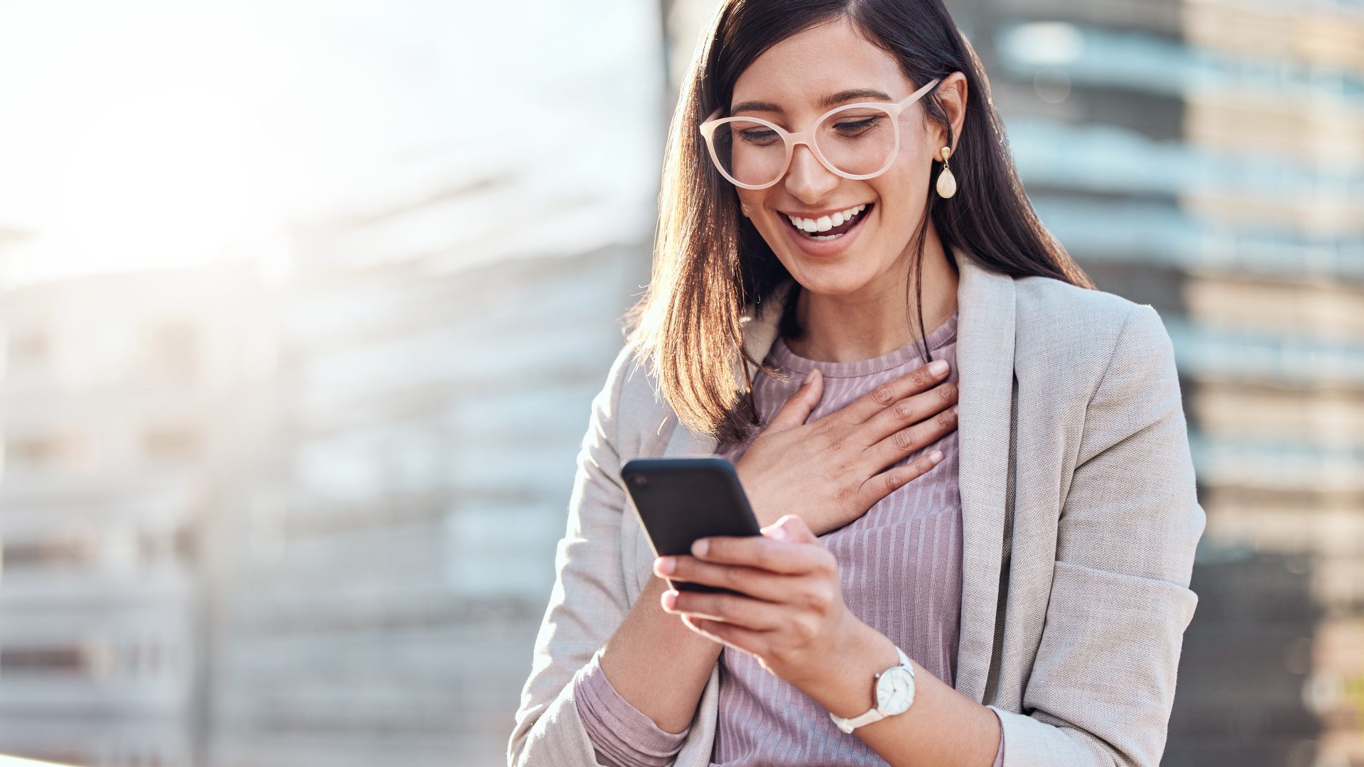 Shot of an attractive young businesswoman standing alone outside and looking surprised while using her cellphone