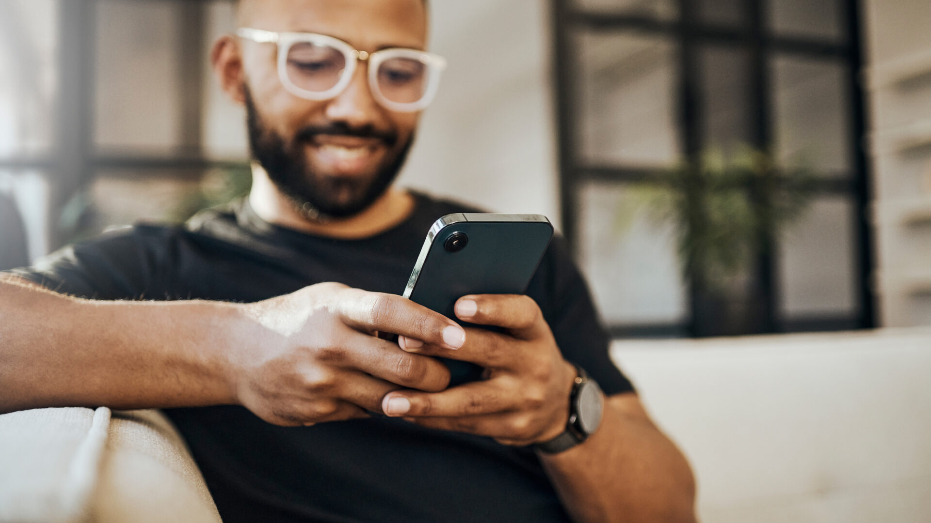 Happy man, social media phone and living room relax, typing smartphone and online communication, reading notification and web on sofa. Smile guy hands, mobile connection and home network technology