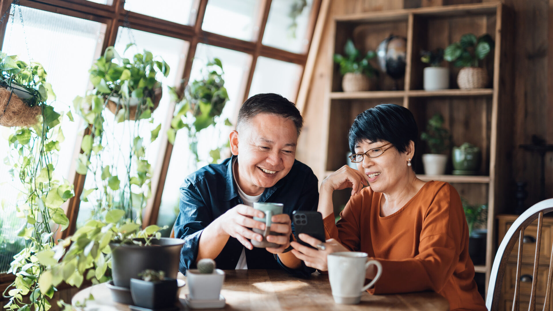 Happy senior Asian couple video chatting, staying in touch with their family using smartphone together at home. Senior lifestyle. Elderly and technology