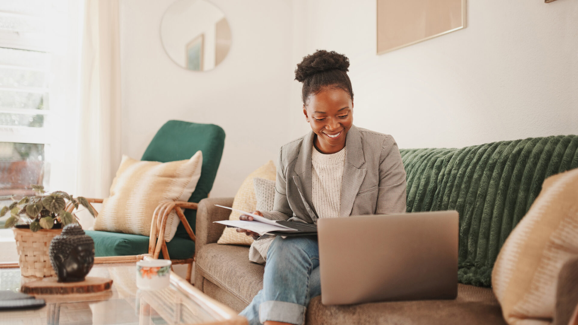 Shot of a young woman using a laptop while going through paperwork at home