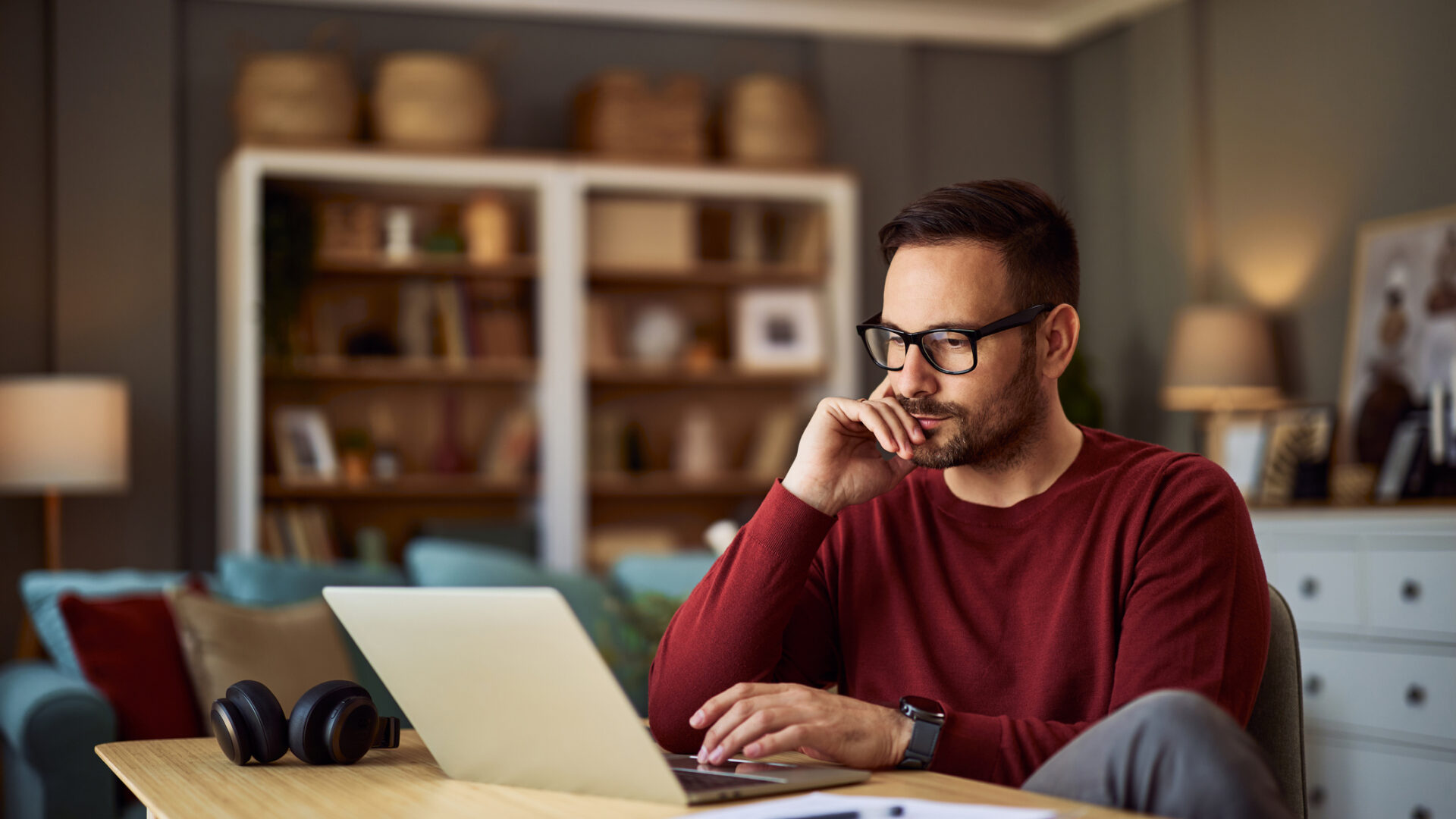 A busy young adult male freelancer resting his head on his hand while working on a project on a laptop.
