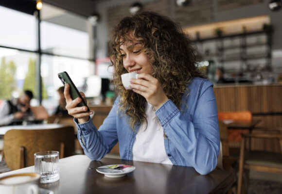Happy young woman using mobile phone and enjoying coffee at cafe