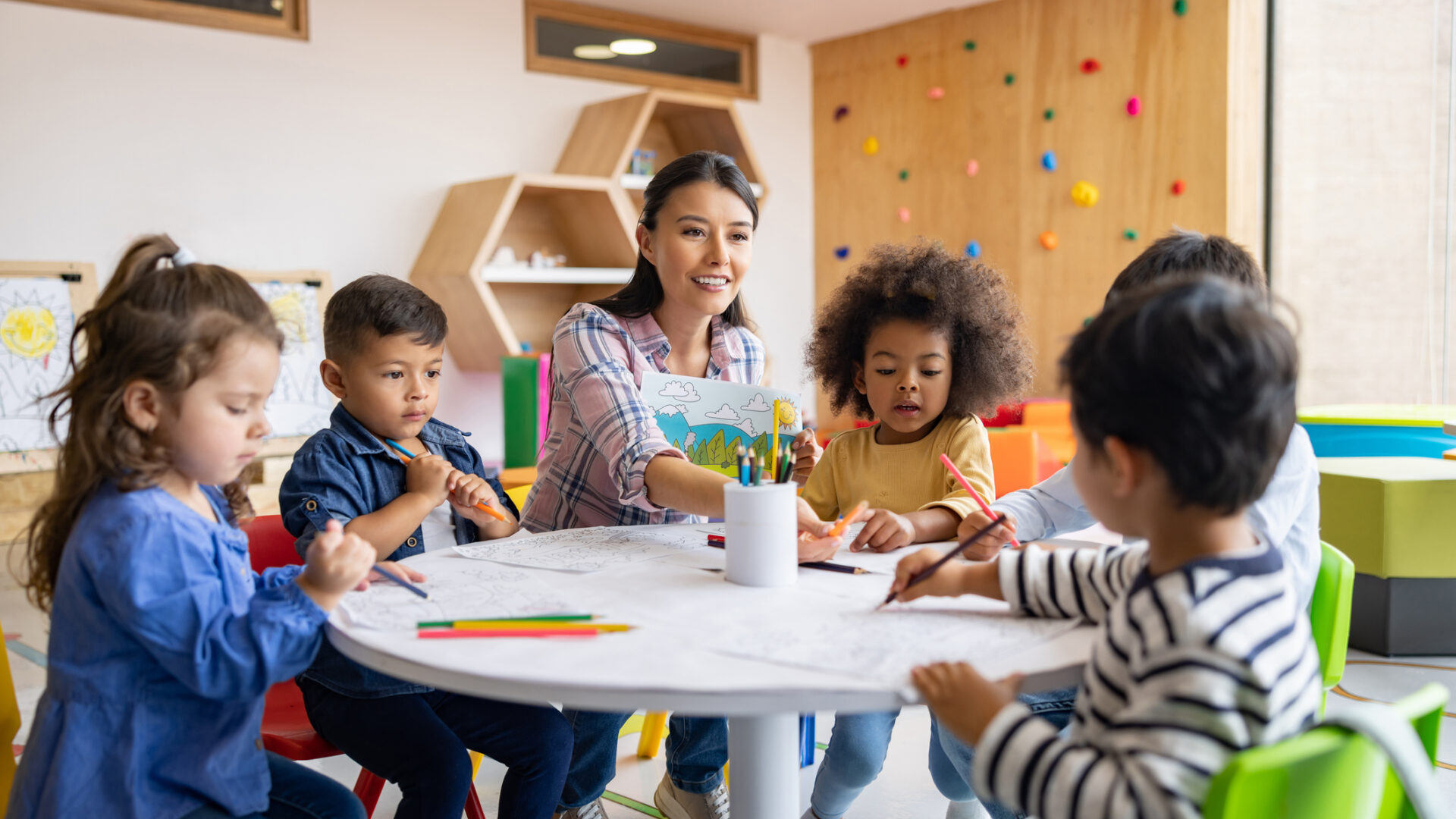 Happy group of Latin American children coloring in art class with the supervision of their teacher - elementary education concepts