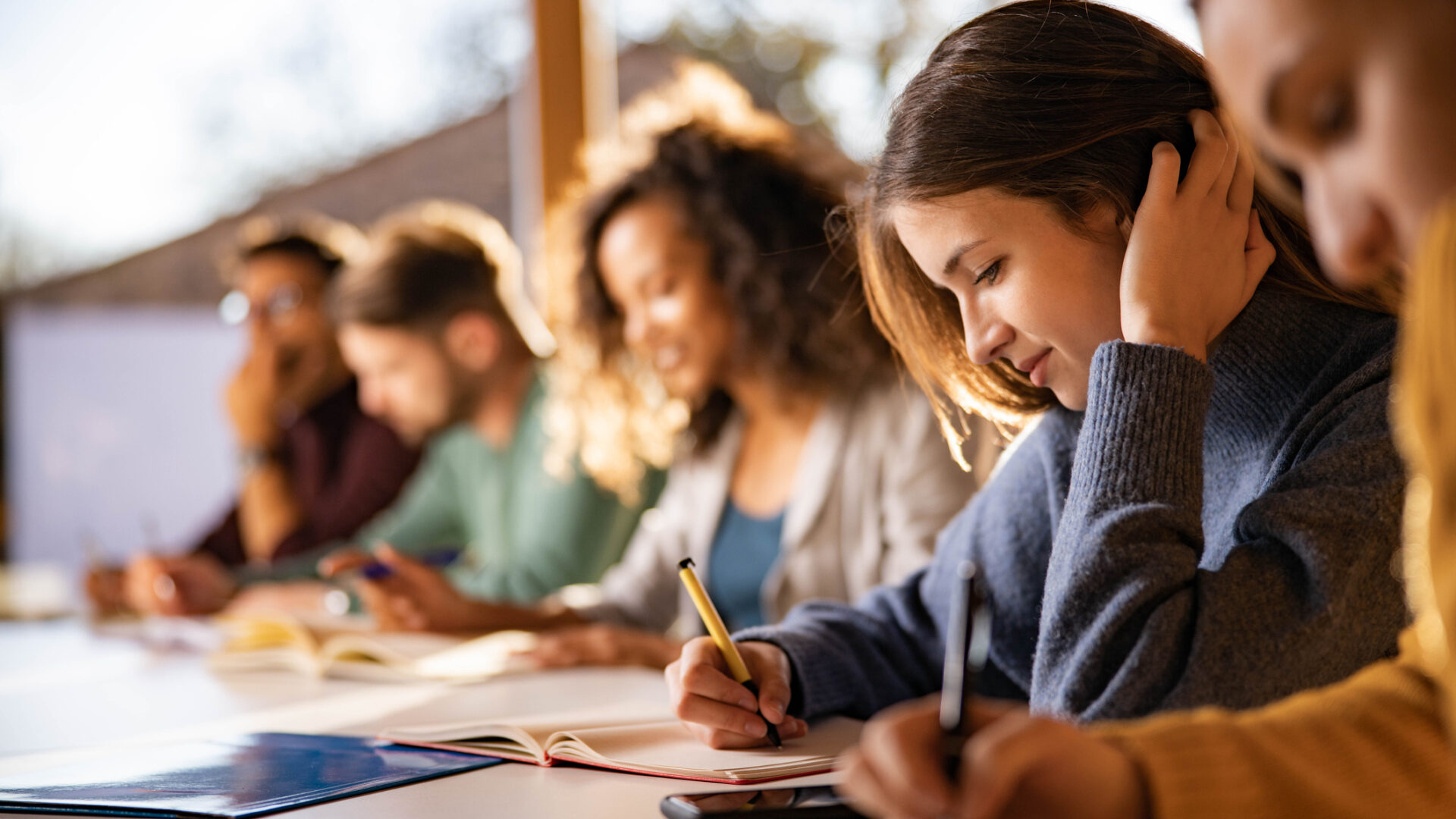 Smiling female student writing an exam while attending a class at college classroom.