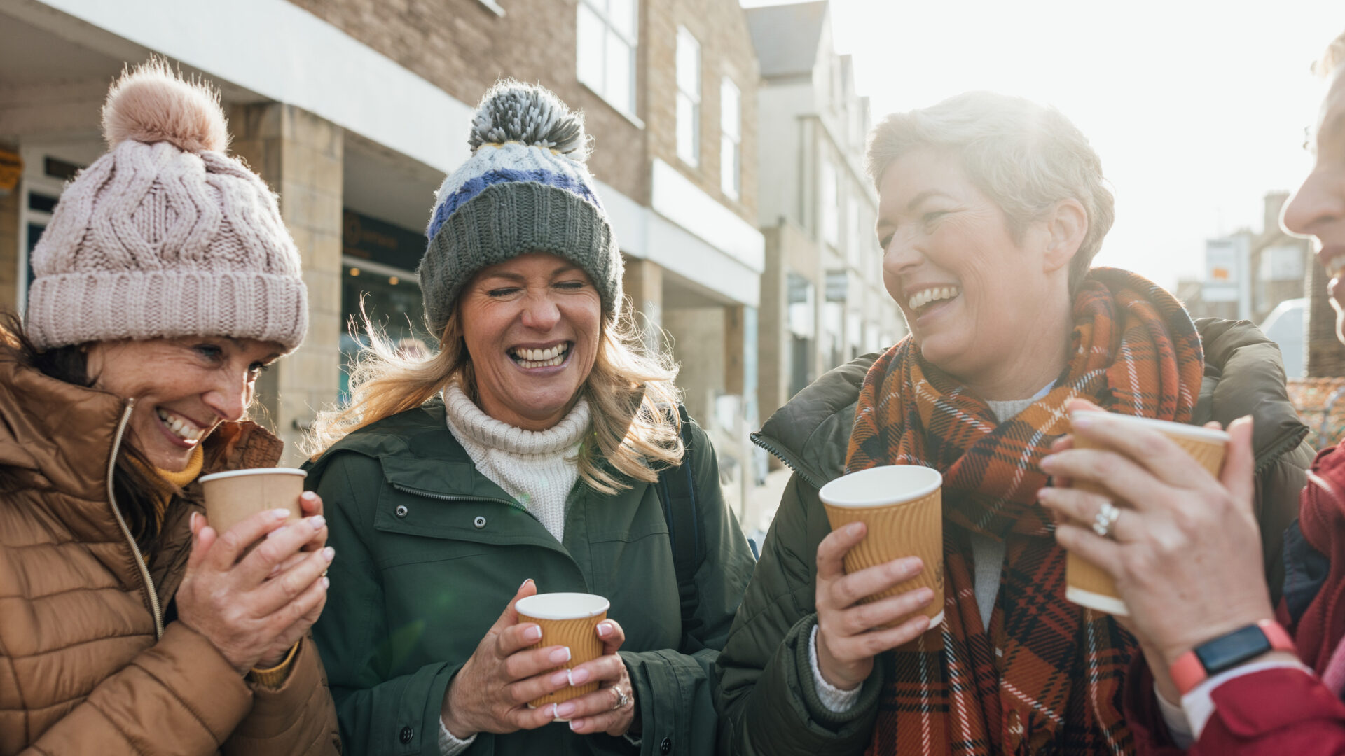 Four women are standing on a street in Seahouses, they are drinking take-out coffee, chatting and laughing.