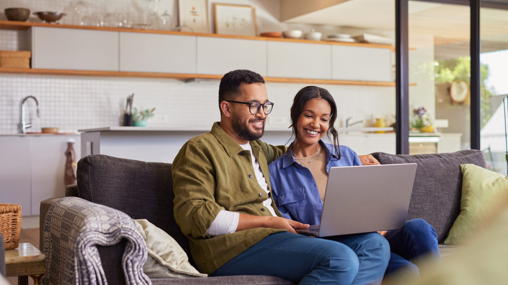 Young mixed race couple watching movie on laptop while relaxing on a weekend at home. Smiling indian man and beautiful woman sitting on sofa while using laptop. Happy mid adult caual man and beautiful hispanic woman sitting on couch while surfing the net.